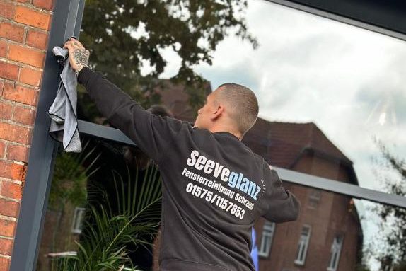 mann von hinten der fenster mit tuch reinigt